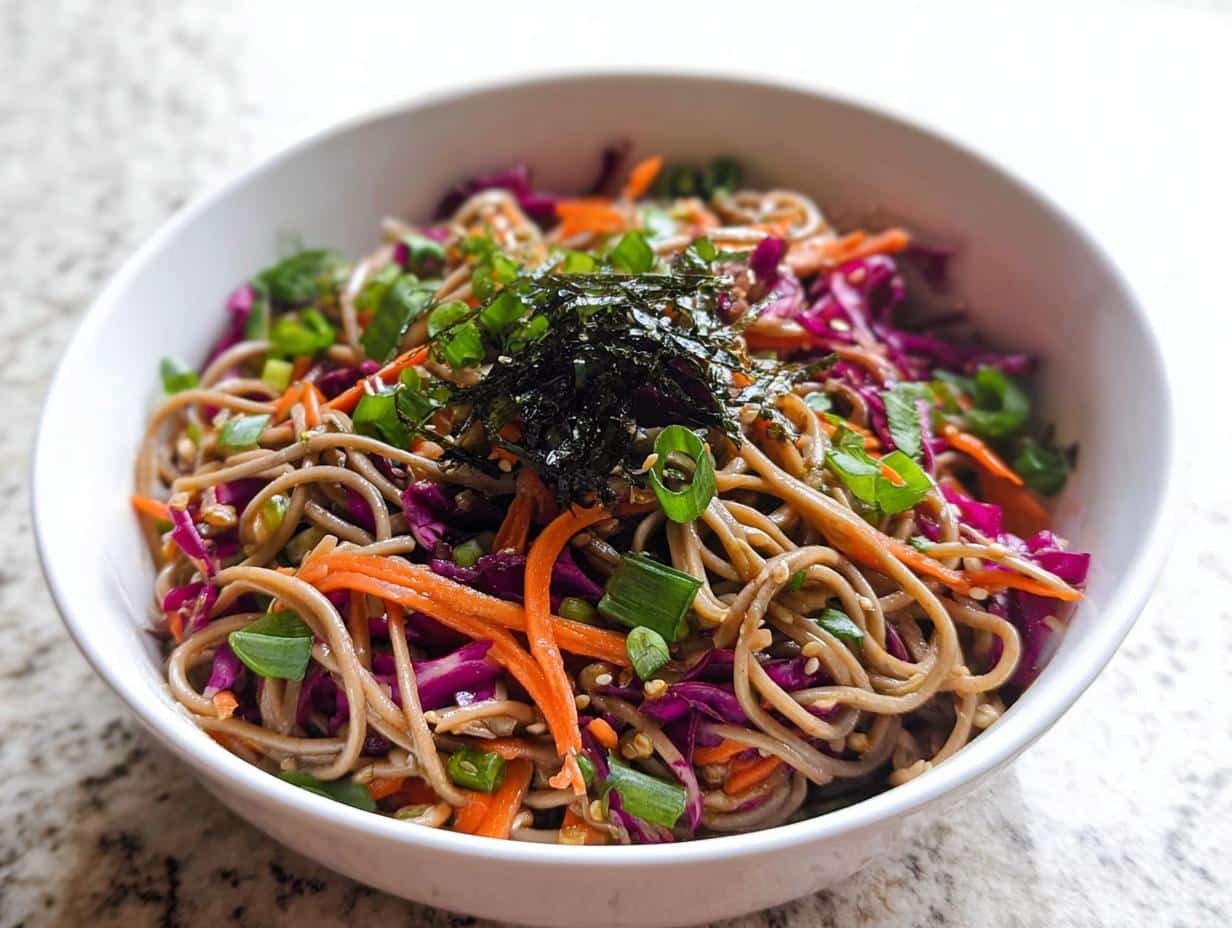 A close-up of a vibrant Cold Soba Noodle Lunch Bowl topped with shredded carrots, red cabbage, and nori.